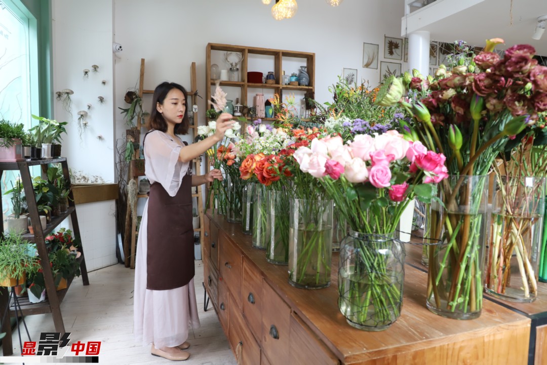 王黎媛是一名河南姑娘，在昆明念完大學后，就再也舍不下春城的藍天陽光、青山碧水，更舍不下這里的四時繁花，于是就干脆留了下來，成了一名媒體人。2017年的時候又毅然辭去工作，創(chuàng)業(yè)開起了花店，成了都市里的一名“花房姑娘”。圖為王黎媛在自己的花店中整理鮮花。新華網(wǎng) 周亞平/攝 念新洪/文